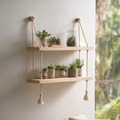 Double tier hanging wooden wall shelf with rope displaying plants on wall